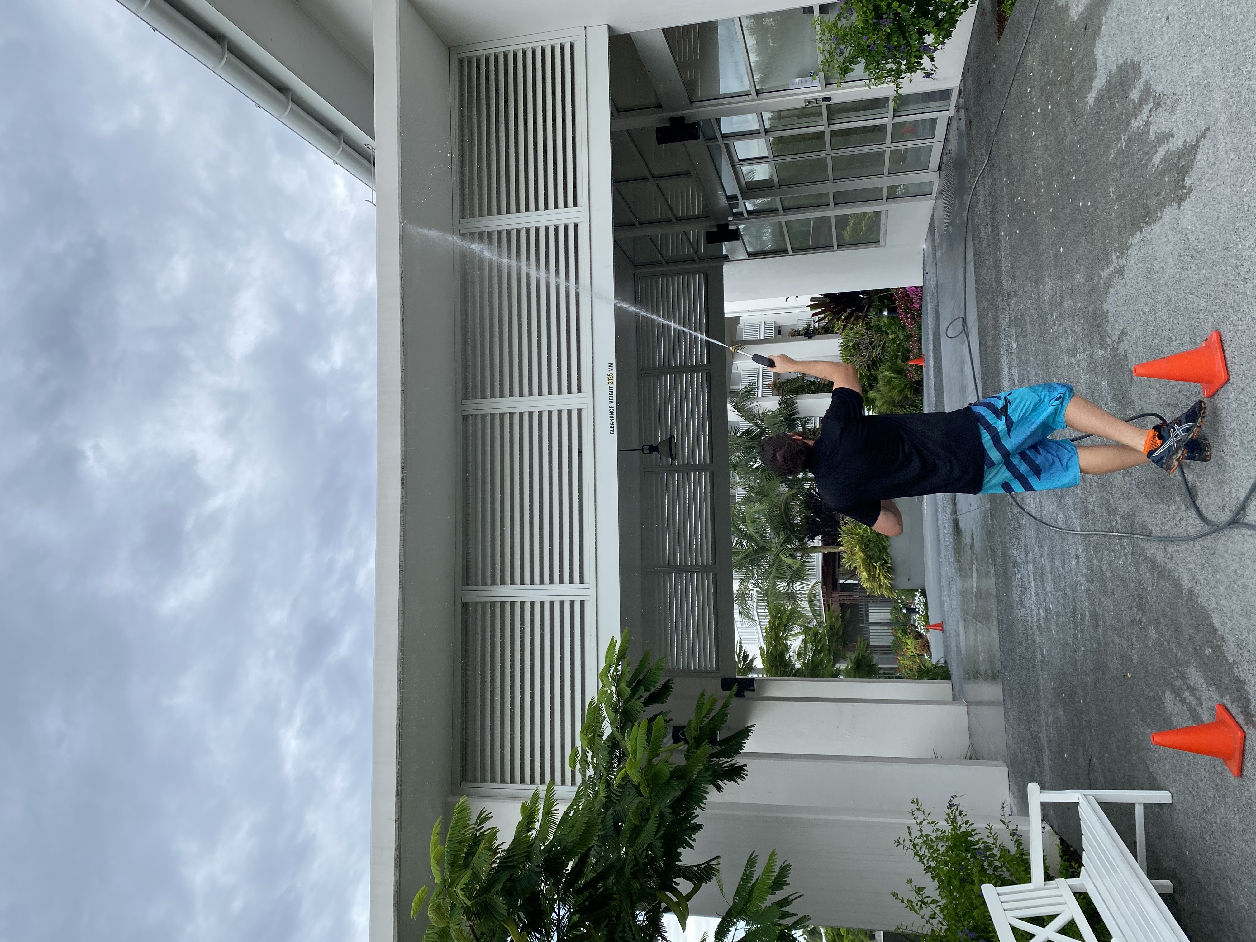Zen worker pressure-cleaning the exterior of a commercial property using a pressure washer, traffic cones placed for safety