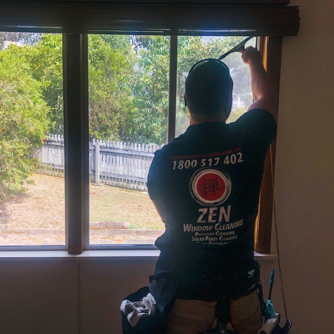 Rhys at work cleaning an interior window, wearing a branded Zen Window Cleaning shirt with the 禅 logo and phone number 1800 517 402