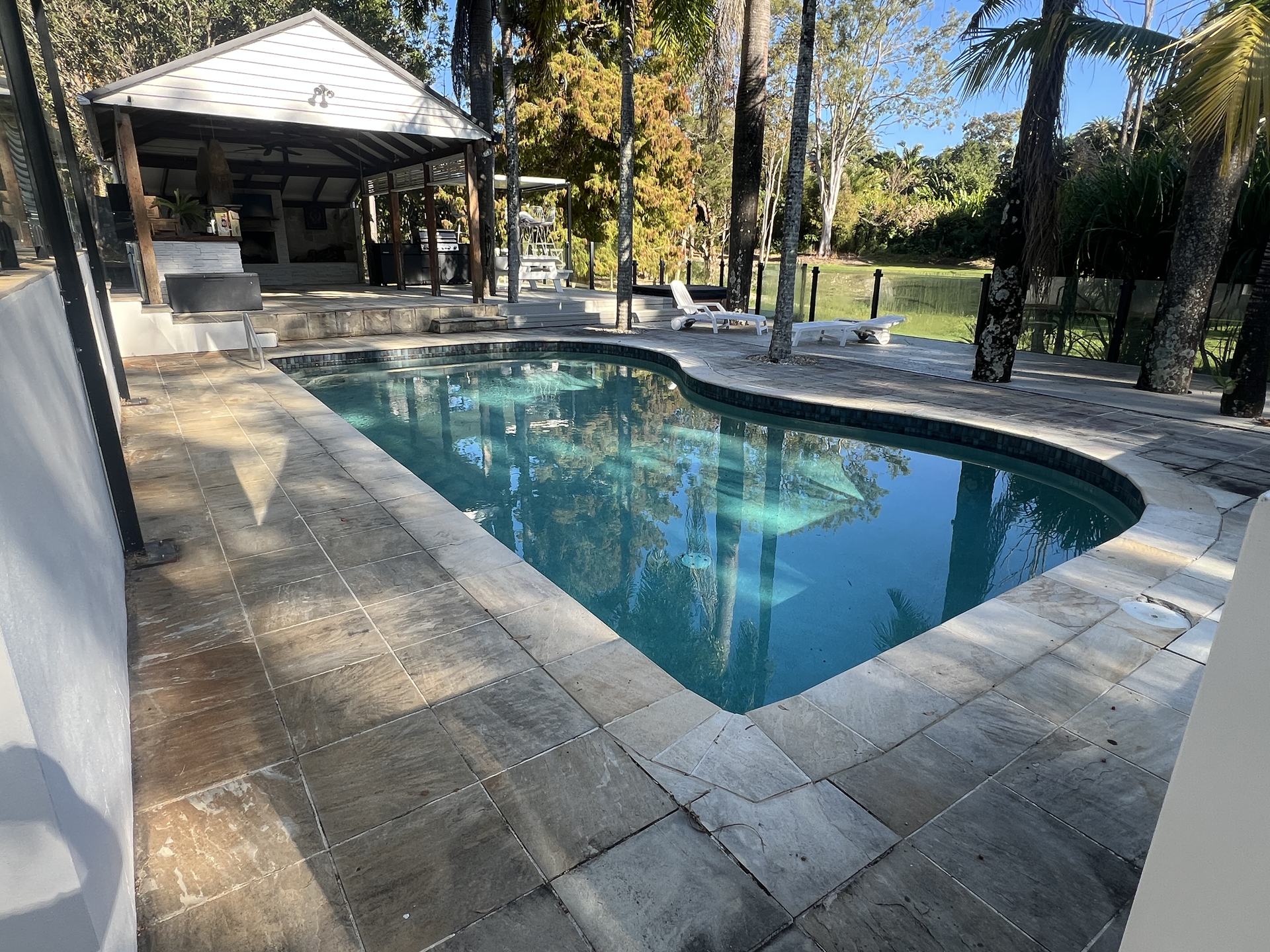Sandstone pool surrounds before pressure cleaning, grey grime and organic staining across the pavers at a Worongary acreage home
