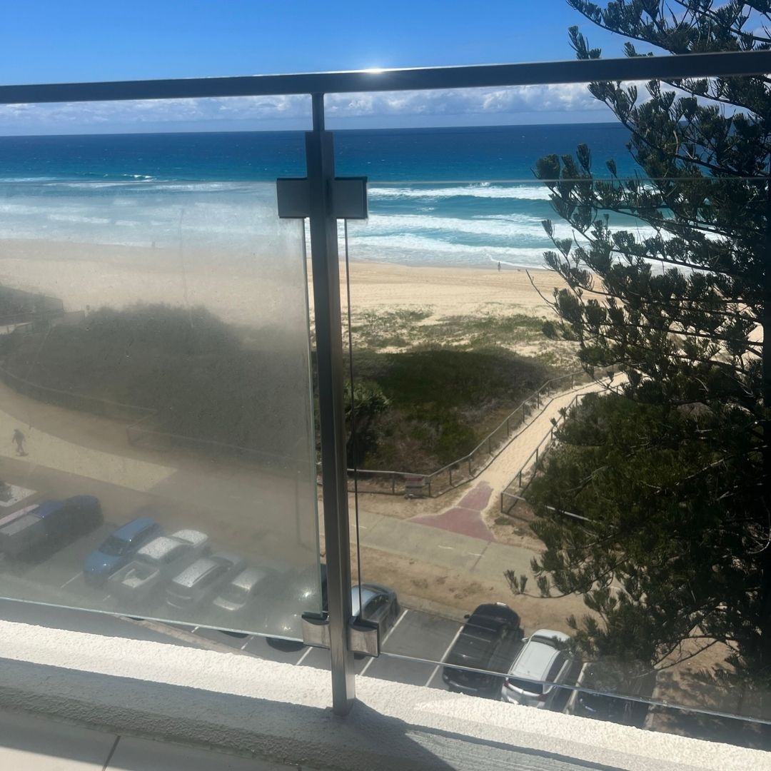 Professional window cleaner working on exterior glass balustrade from inside high-end Gold Coast unit
