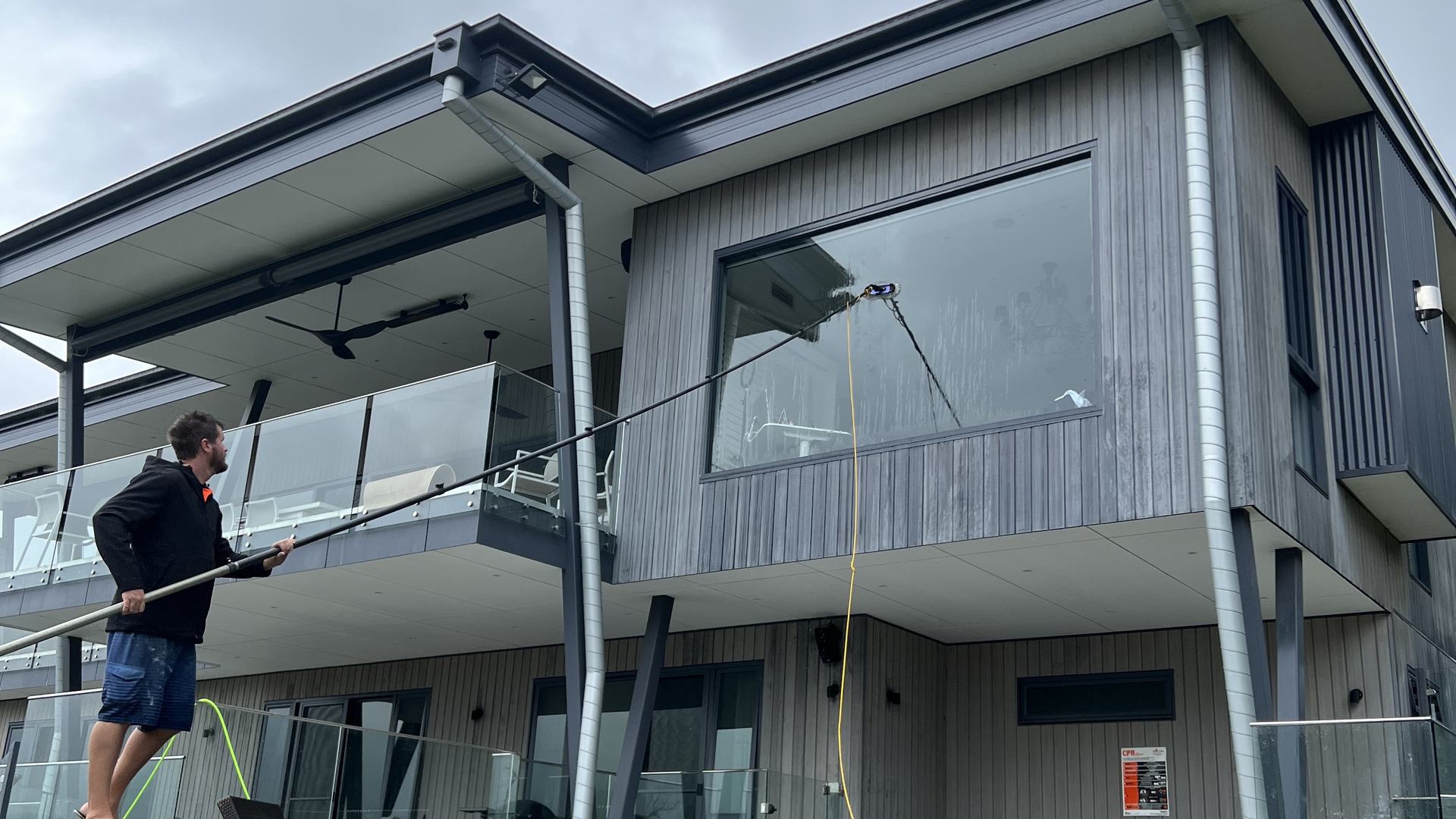 Rhys cleaning the upper windows of a modern home on Tamborine Mountain with a water-fed pole